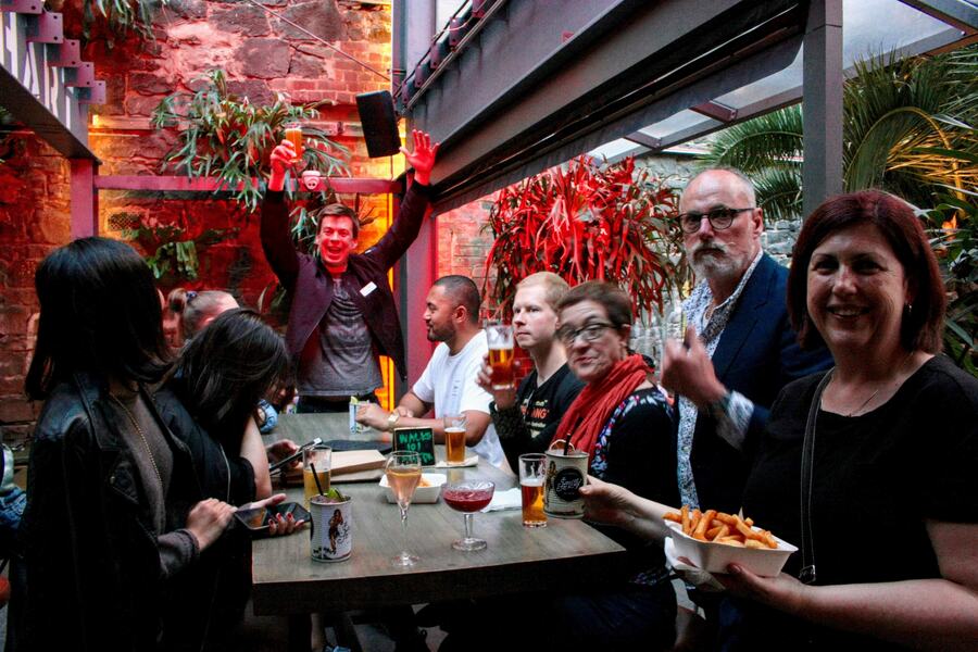 A guide raising a glass with guests in a laneway bar courtyard at night