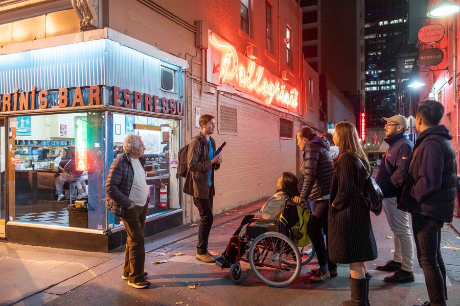 A guide talking to a group outside Pellegrini's at night, a guest in a wheelchair among them